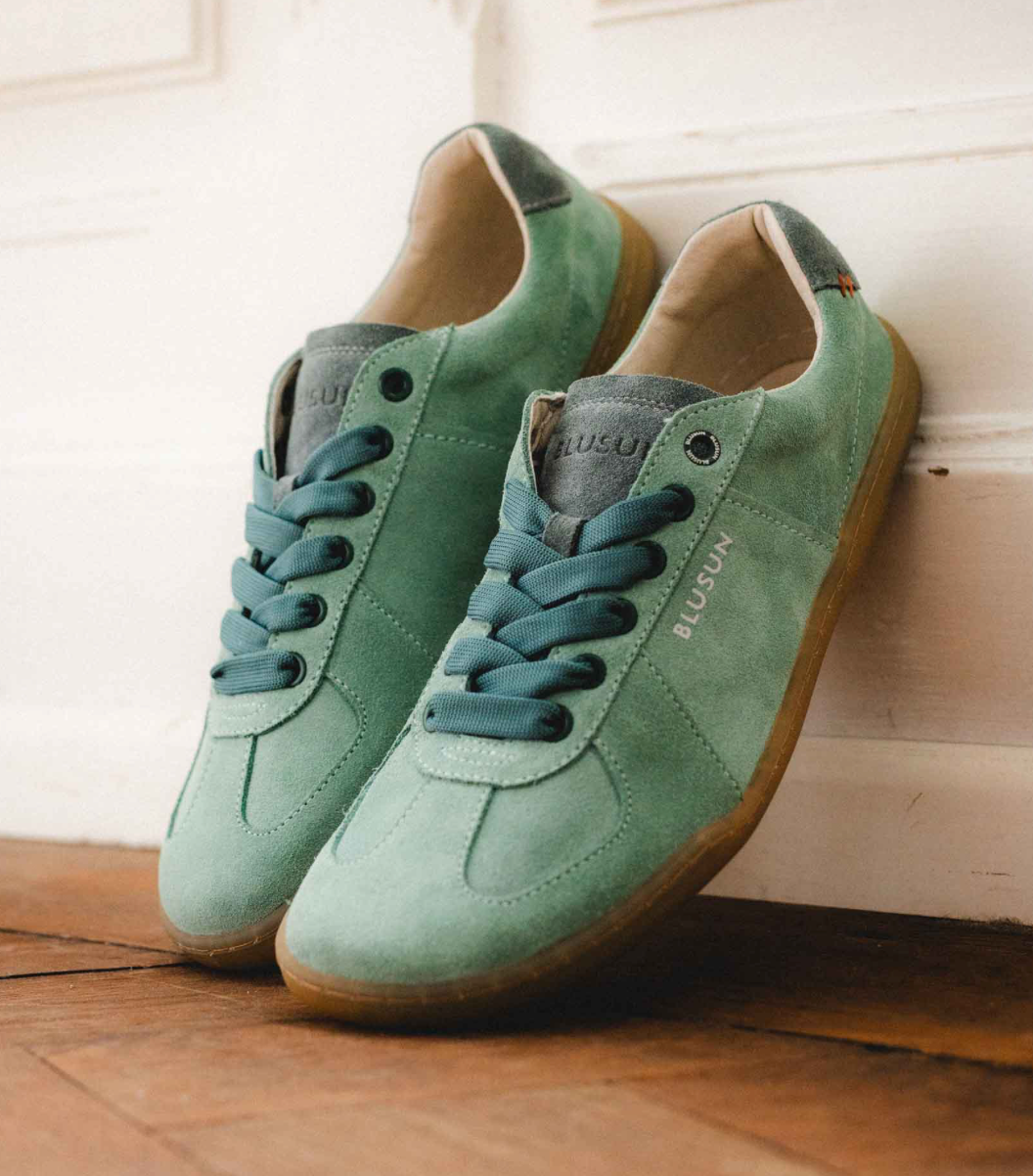 Blusun Sneaker green jade sage grün komplett aus Velour Leder, mit etwas dunkler grünen Schnürsenkeln, laces, and der Ferse und an der Zunge grauer Kontrast. Die Sohle ist Honig farbig und sehr dünn für's Barfußgefühl. Foto von hinten, ein Paar steht schräg an der Wand, lässiges Foto.