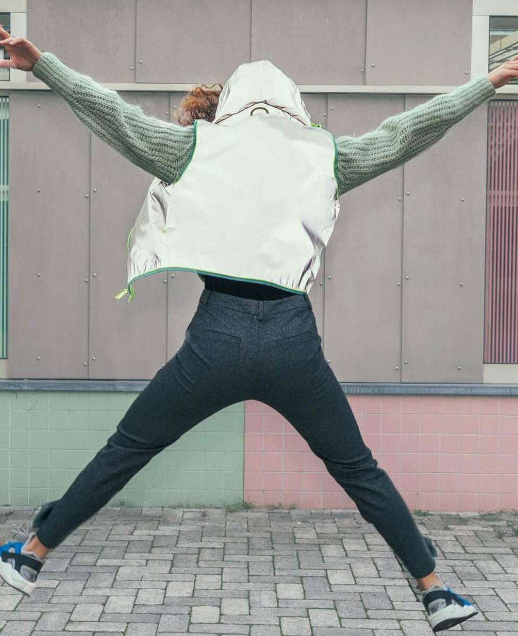 Warnweste GoFluo Go Fluo Darknight Reflektorweste Warnweste mit Reißverschluss 2-Wege Reißverschluss und Kapuze, springende junge Frau von hinten, Arme hoch geschwungen